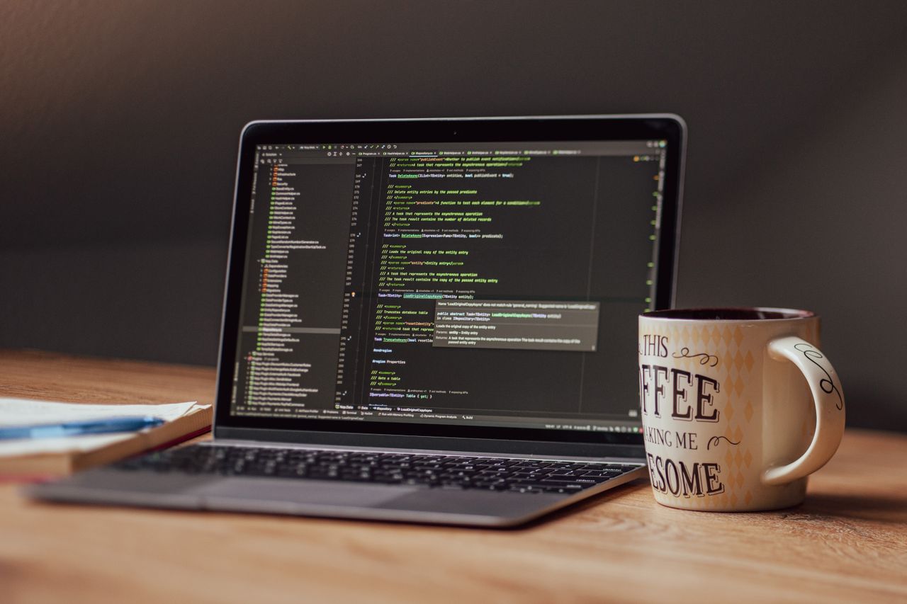 A laptop showing an IDE with code open, coffee beside it.